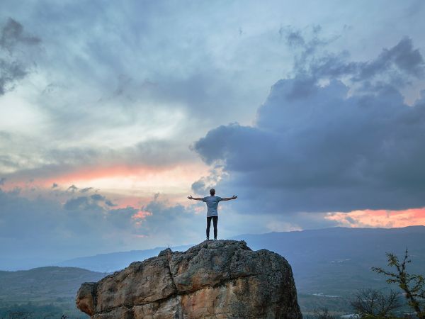 Un homme en haut d'un grand rocher respire à pleins poumons face à un beau paysage